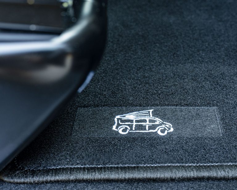 Von Fahrer- bis Beifahrersitz durchgehnde Premium Fußmatte mit gesticktem Logo.